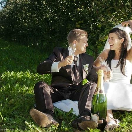 Ein Brautpaar sitzt in einem Obstgarten und hält Sektgläser in der Hand, um ihren besonderen Moment zu feiern.