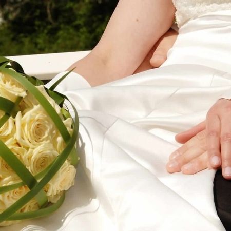 Ein Brautpaar sitzt auf einer Bank und hält Händchen, umgeben von einer romantischen Atmosphäre.