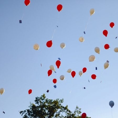 Viele rote, weiße und blaue Ballons schweben am Himmel und verleihen der Szenerie eine festliche Atmosphäre.