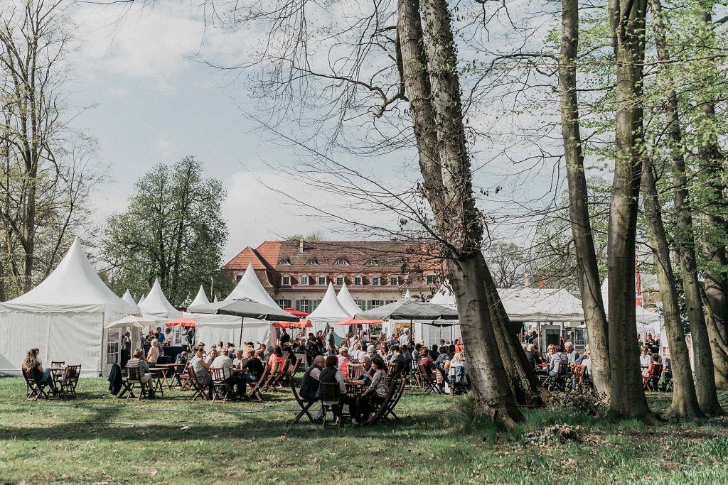 Eine große Gruppe von Menschen sitzt an Tischen in einem Park und genießt die Zeit im Freien.