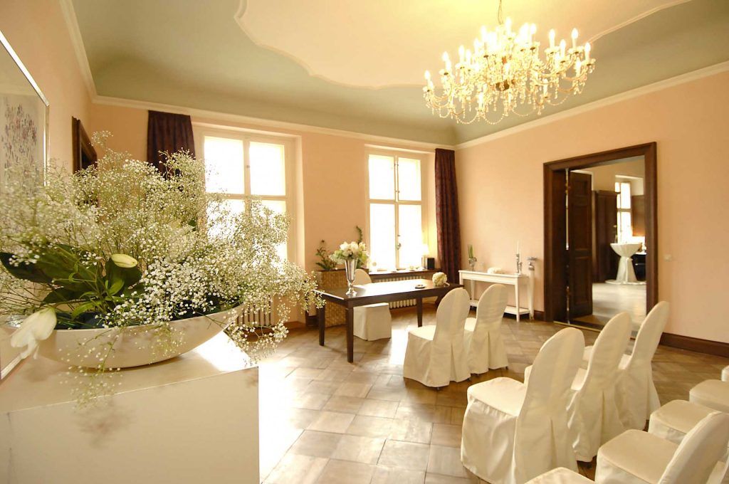 Ein Hochzeitszeremonie-Raum mit weißen Stühlen und Blumenarrangements, festlich und elegant dekoriert.